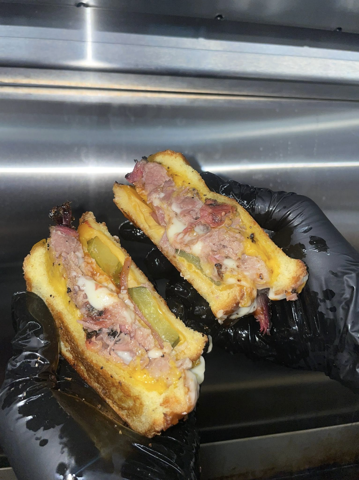 Two halves of a grilled BBQ melt with pickles
